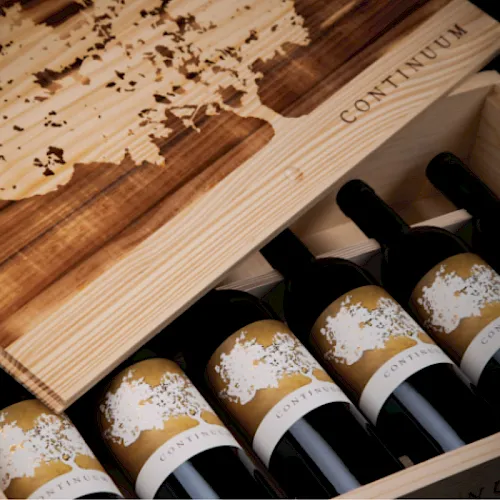 A wooden wine crate holds several Continuum bottles with gold labels and corked glass.