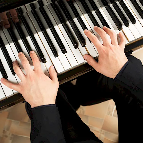 Hands playing a piano keyboard, pressing white and black keys in a warm indoor setting.