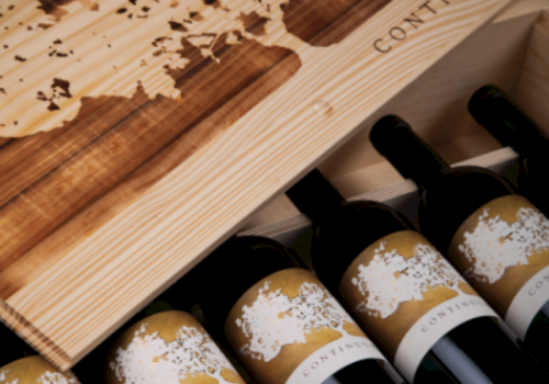 A wooden wine crate holds several Continuum bottles with gold labels and corked glass.