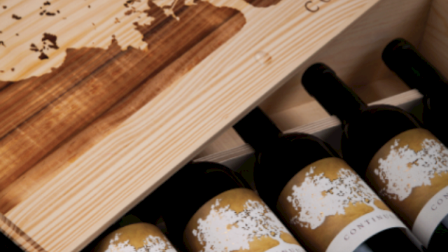 A wooden wine crate holds several Continuum bottles with gold labels and corked glass.