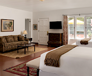 A bright bedroom with a large bed, patterned curtains, a wall TV, and a sofa in the lounge area.