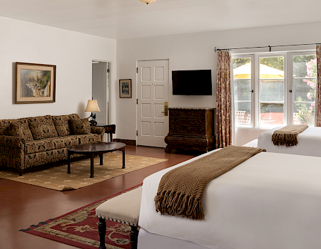 A bright bedroom with a large bed, patterned curtains, a wall TV, and a sofa in the lounge area.