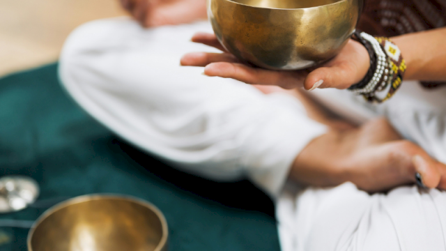 A healing scene: hands hold brass singing bowls for sound therapy, with a person preparing to play them during a calm session.