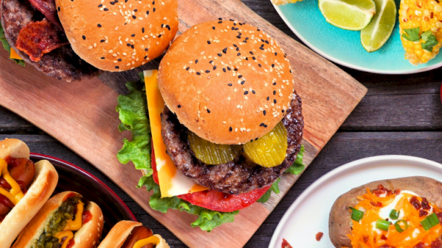 The image shows burgers and hot dogs with sides like corn, pickles, cheese, and lime wedges on plates.