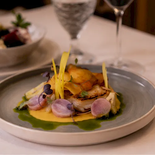 A plated gourmet entr&eacute;e with green pur&eacute;e, seared fish, radish slices, and yellow edible stems on a silver dish.