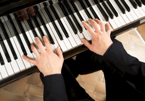 Hands playing a piano keyboard, pressing white and black keys in a warm indoor setting.