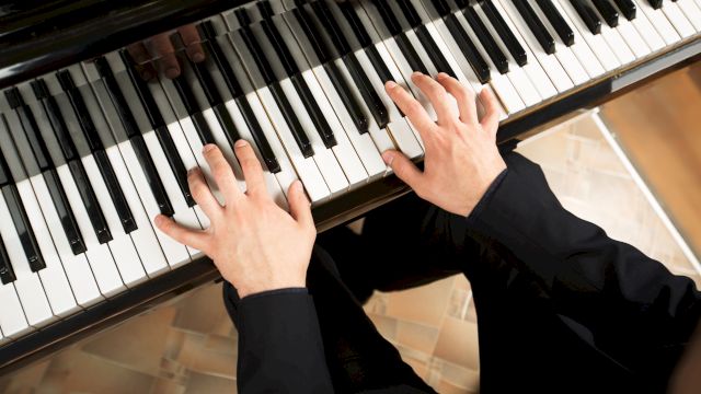 Hands playing a piano keyboard, pressing white and black keys in a warm indoor setting.