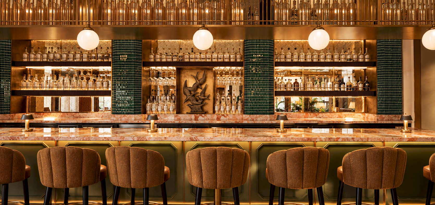 A luxurious bar interior with marble counter, glowing lights, shelves of liquor bottles, and cushioned stools behind a green tiled backdrop.