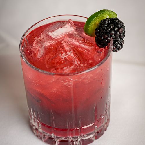 A glass of icy red berry drink topped with a lime wedge and blackberries.