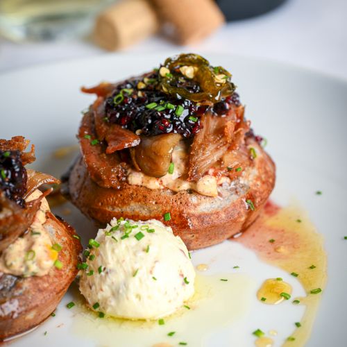 Close-up of a plated roast with creamy sauce, herbs, and a dark peppery relish topping over sliced meat.