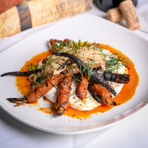 A plated seafood dish&mdash;shrimp and squid over creamy sauce, garnished with dill&mdash;beside decorative chess pieces on a table.
