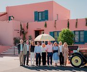 A group poses for a photo outside the Arizona Inn, in front of a pink building, with an umbrella and vintage car nearby.