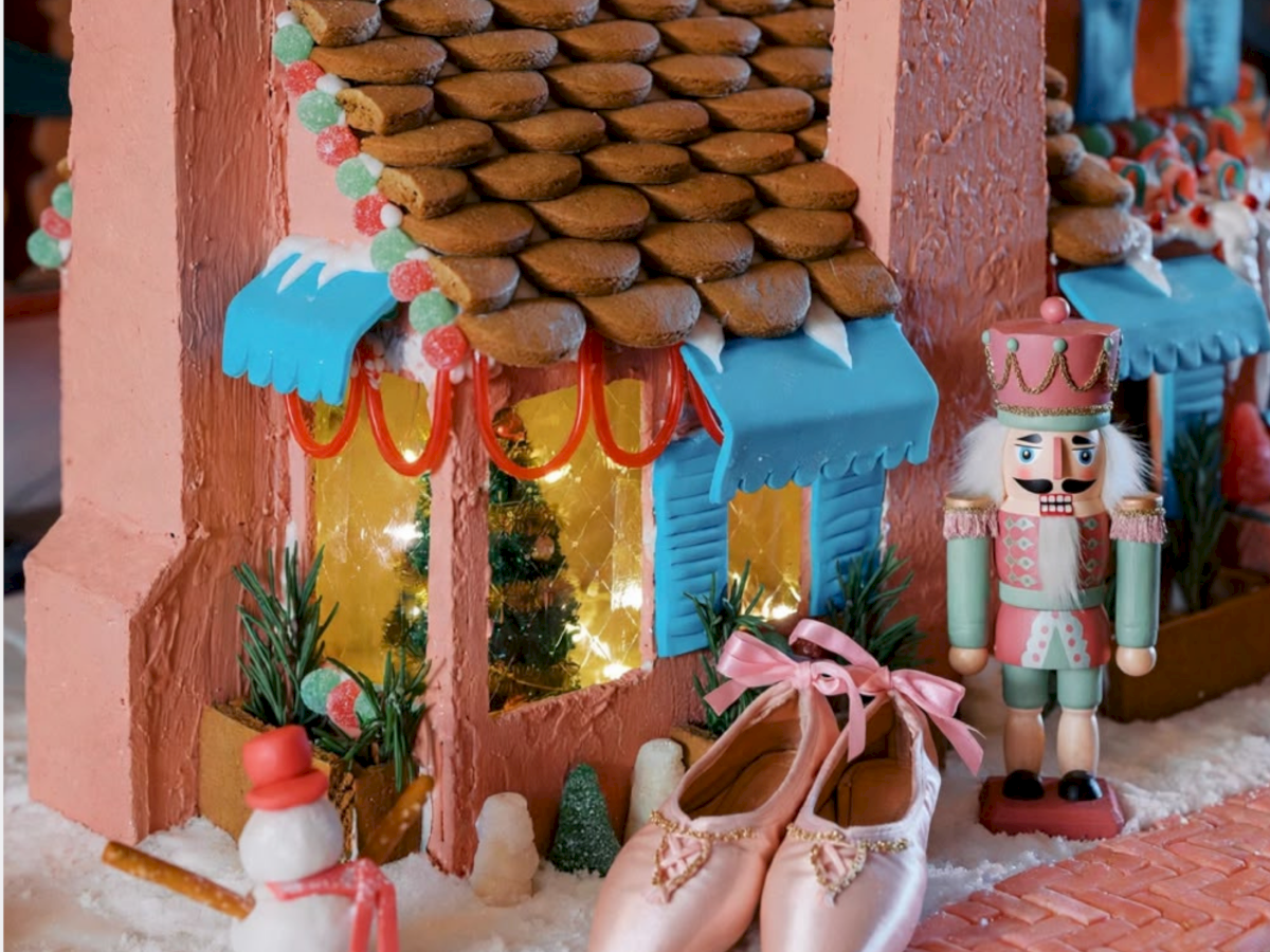 A festive gingerbread-style house with candy decorations, cookies, and a nutcracker figurine stands in the snow.