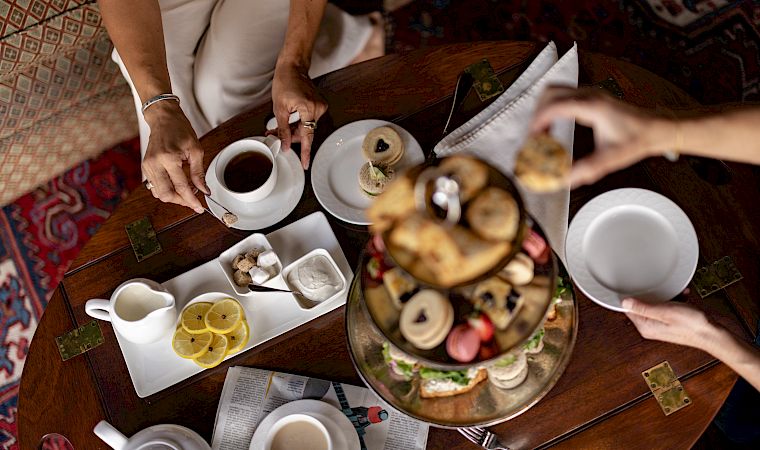 A group breakfast at a wooden table with teacups, pastries/danishes, and people serving coffee and sweets.