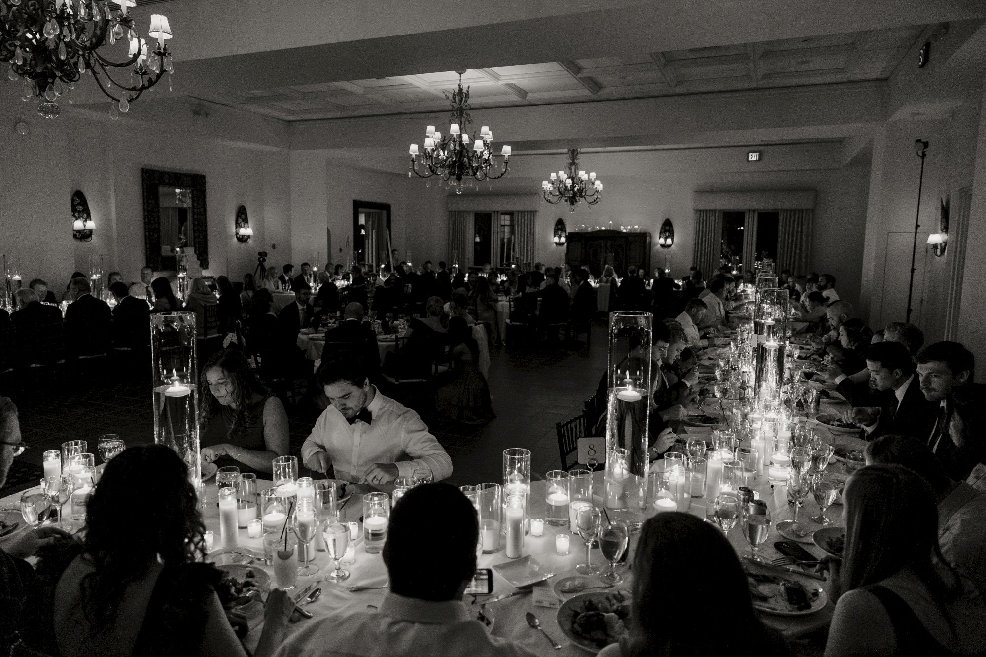 A formal dinner event with many guests seated at long tables, candles lit, and a chandelier-lit room.