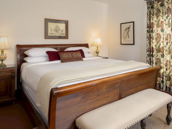 A cozy, classic hotel bedroom with a wooden four-poster bed, white linens, decorative pillows, matching nightstands, lamps, and a bench by the footboard.