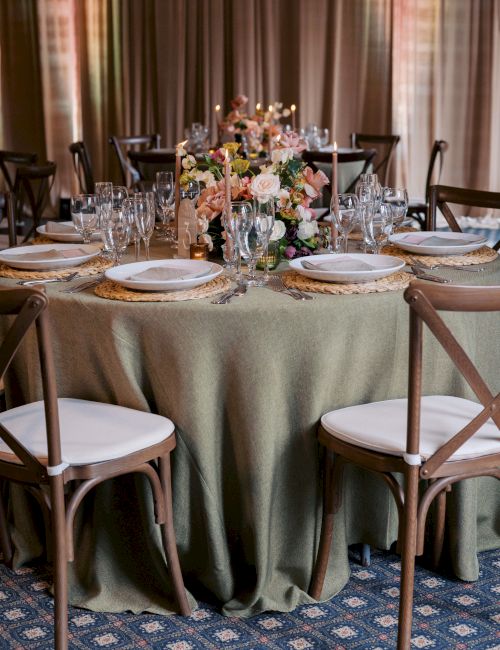A wedding/banquet table set with candles, glassware, plates, and a lush floral centerpiece glowing with warm light.