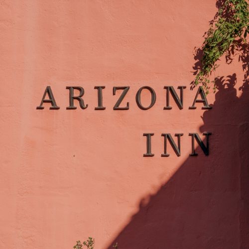 Arizona Inn sign on a peach-colored wall with a shadow and some greenery at the corner.