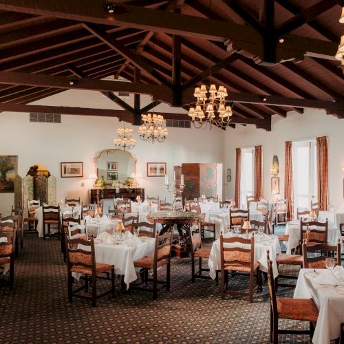 A large, upscale dining room with round tables, white linens, and ornate chandeliers in a classic, elegant setting.