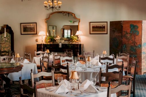 Elegant restaurant dining room with white-tablecloth tables, chandeliers, and framed art, set for a meal.