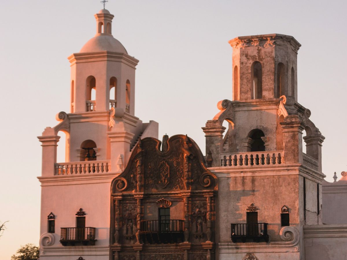 A historic church facade with two bell towers, warm sunset light, and decorative stonework, set against a clear evening sky.