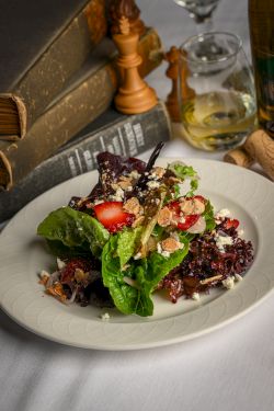 Fresh salad with mixed greens, strawberries, toasted nuts, and crumbled cheese on a white plate &mdash; a colorful, elegant dish.