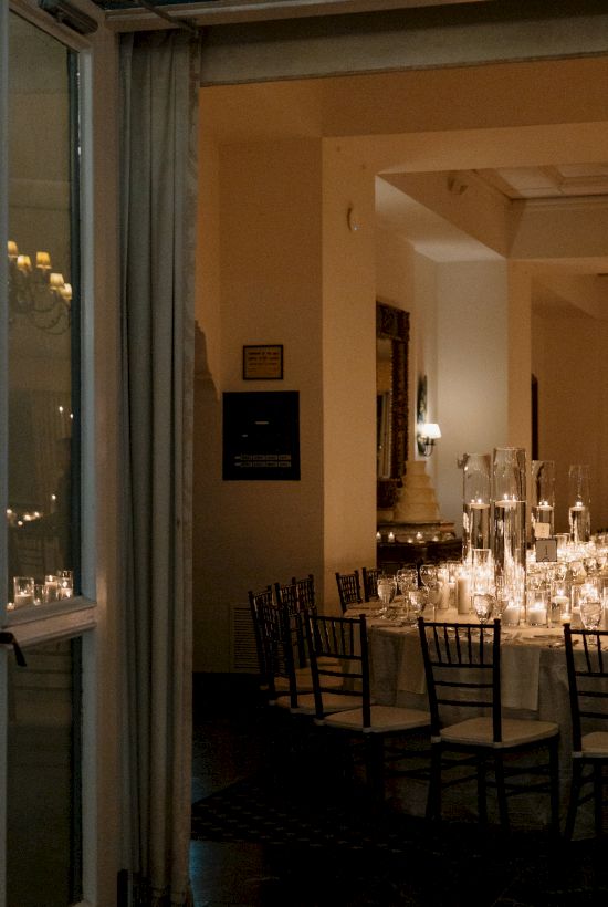 An elegant dining room seen through a doorway, candles and white-lit tables create a warm, intimate ambiance for a formal meal.