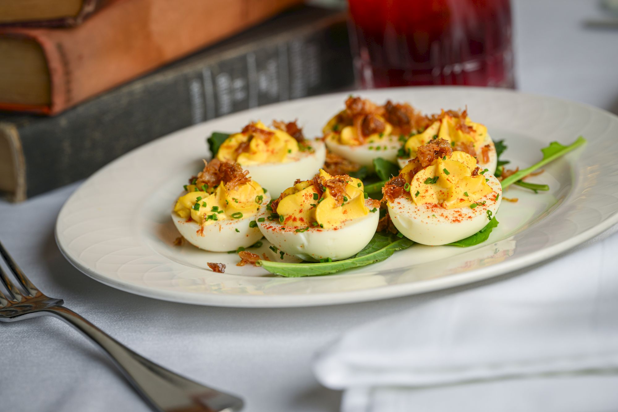 A plate of deviled eggs topped with herbs and bacon bits, arranged on a white plate with a fork nearby, ready to serve.
