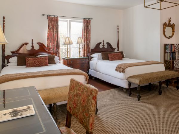 Two large, classic wooden beds with matching headboards, lamps, a patterned bench, and vintage decor in a warm, traditional hotel room.