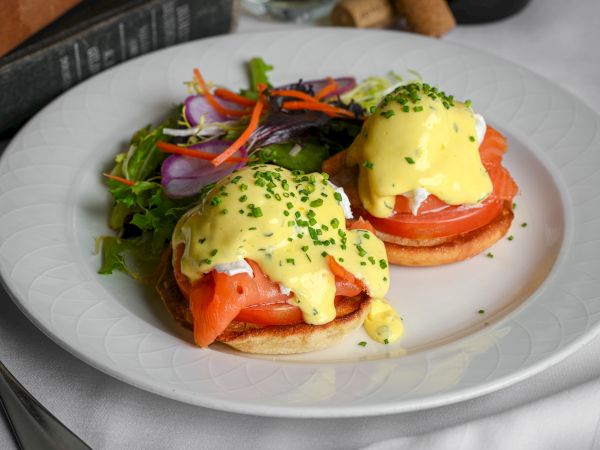 Two poached eggs? Actually eggs benedict with hollandaise over tomato slices on a plate, plus salad greens on the side. It&rsquo;s a plated breakfast.