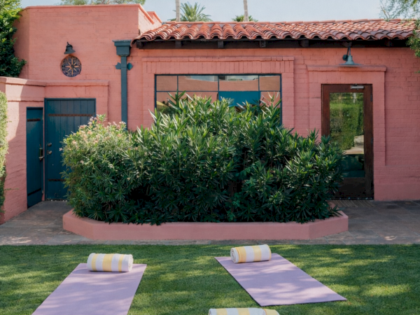 A pink stucco building with a tiled roof, green doors/windows, manicured lawn, yoga mats and rolled towels on the grass for outdoor exercise.