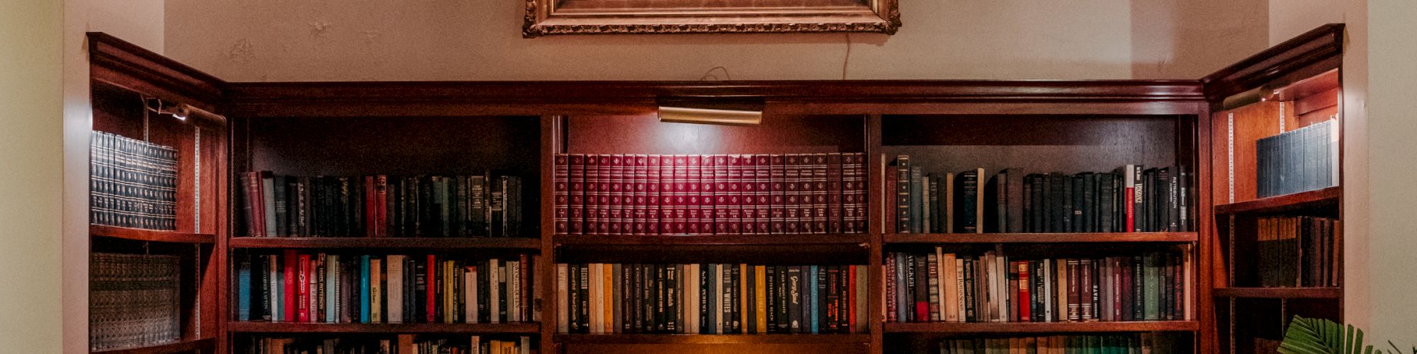 A cozy library nook with tall wooden shelves full of books, a central table with a lamp, and a framed portrait above, warm, inviting ambience.