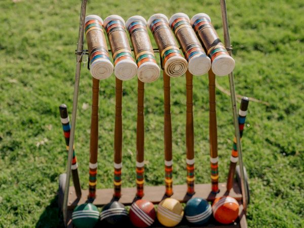 A set of colorful croquet mallets and balls neatly arranged on the grass, ready for a sunny game.