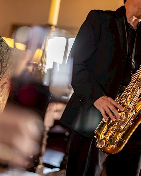 A saxophonist playing live jazz in a cozy venue, with blurred foreground d&eacute;cor and warm lighting.