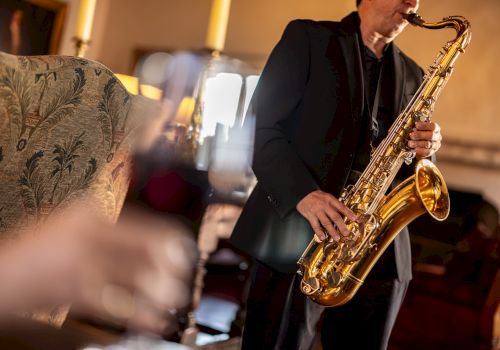 A saxophonist playing live jazz in a cozy venue, with blurred foreground d&eacute;cor and warm lighting.