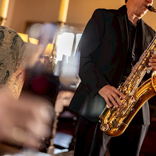 A saxophonist playing live jazz in a cozy venue, with blurred foreground d&eacute;cor and warm lighting.