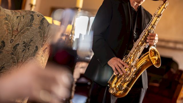 A saxophonist playing live jazz in a cozy venue, with blurred foreground d&eacute;cor and warm lighting.