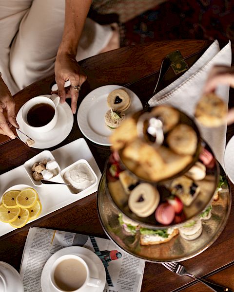 A cozy tea-time scene with friends sharing coffee, pastries, and fruit on a decorative table spread, inviting conversation and smiles.