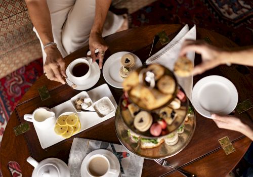 A cozy tea-time scene with friends sharing coffee, pastries, and fruit on a decorative table spread, inviting conversation and smiles.