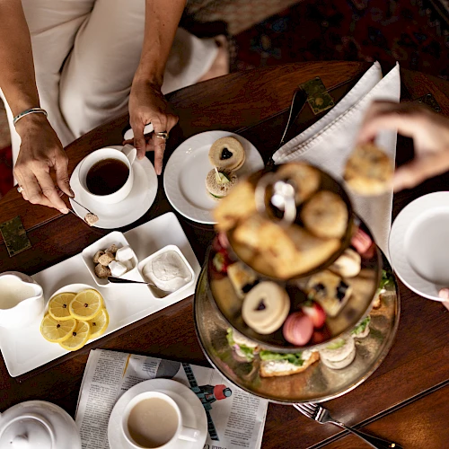 A cozy tea-time scene with friends sharing coffee, pastries, and fruit on a decorative table spread, inviting conversation and smiles.