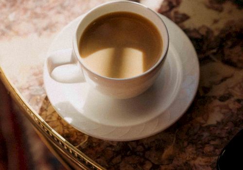 A cup of coffee on a saucer atop a marble table, warm amber liquid inviting a quiet morning moment.