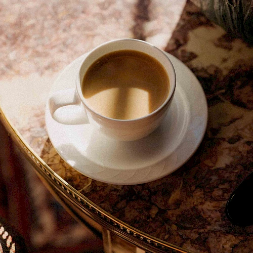 A cup of coffee on a saucer atop a marble table, warm amber liquid inviting a quiet morning moment.