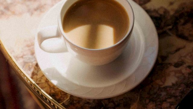 A cup of coffee on a saucer atop a marble table, warm amber liquid inviting a quiet morning moment.
