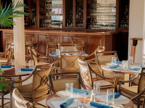 A cozy cafe interior with wooden chairs, round tables set with blue napkins and glasses, a vintage bar in the background, warm lighting.