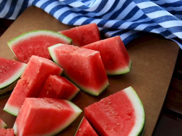 Sliced watermelon wedges on a wooden board, with a blue-and-white striped cloth nearby, perfect for a refreshing summer snack.