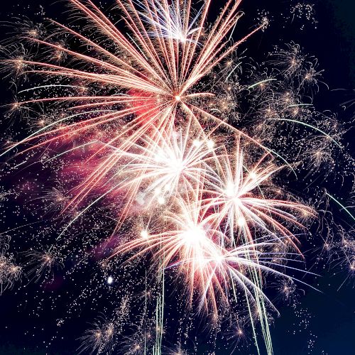 Fireworks exploding in the night sky, bright bursts and trails illuminating the dark backdrop.