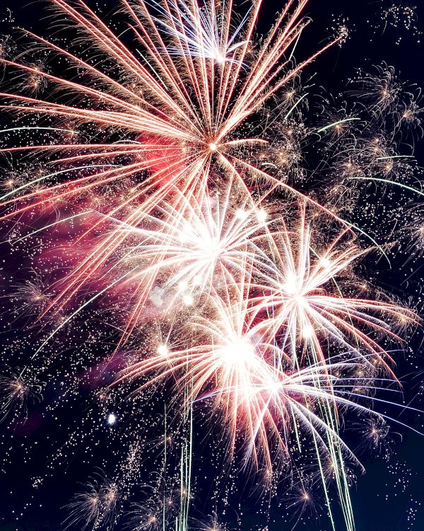 Fireworks exploding in the night sky, bright bursts and trails illuminating the dark backdrop.