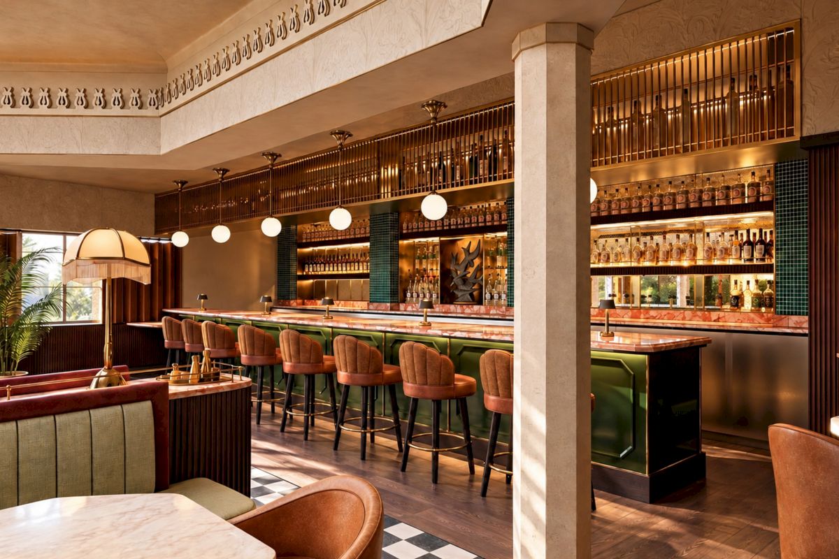 A stylish hotel bar with a marble counter, warm pendant lights, and rows of liquor bottles behind glass.