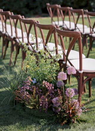 Outdoor event setup with brown folding chairs around a grassy area, framed by lush green plants and purple flowers.