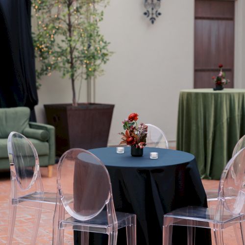 An outdoor table set for an event with clear chairs, a flower centerpiece, drinks, and soft wall lantern lighting.